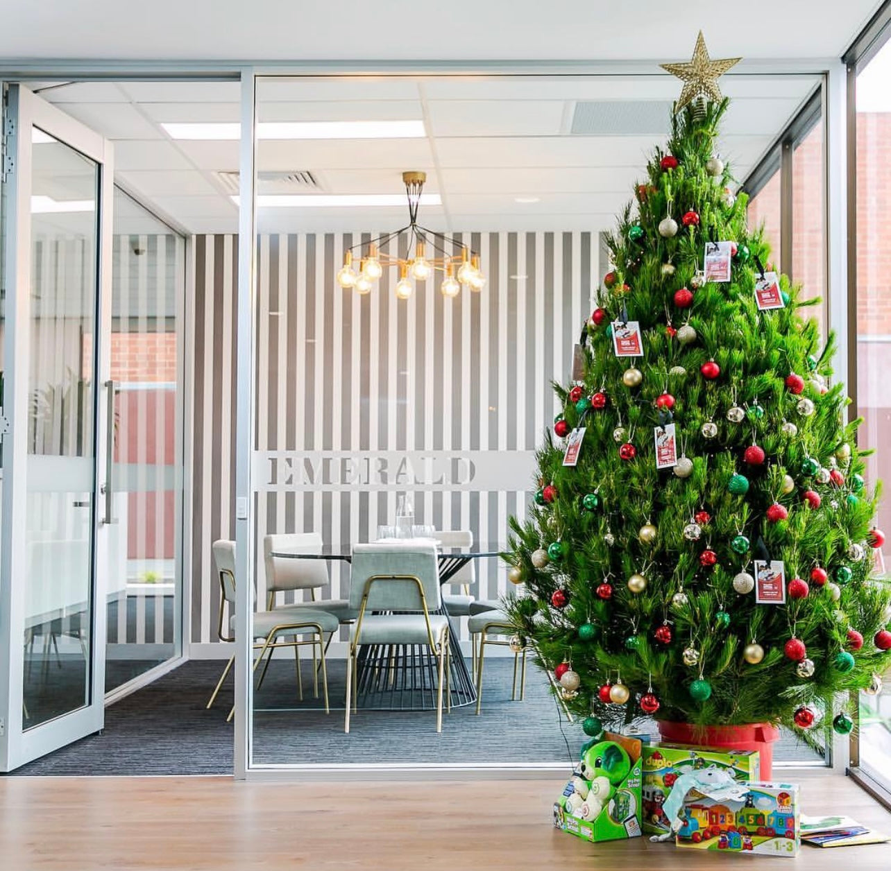 Real Christmas tree in office space, decorated with ornaments and gifts underneath. Fresh and bushy Christmas tree from local Christmas tree farm, perfect for bringing holiday spirit. Delivered by Santas Trees